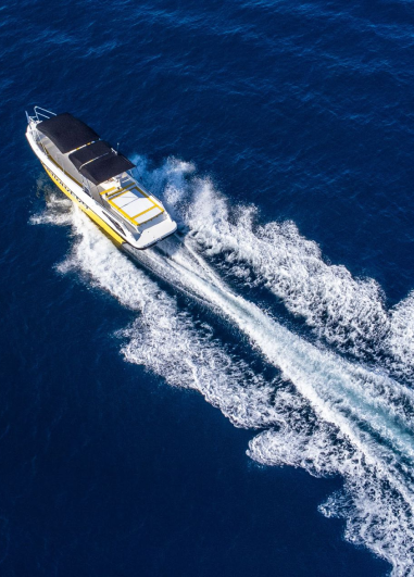 Aerial view of a speedboat with a yellow and white design cutting through deep blue water, leaving a foamy wake behind.
